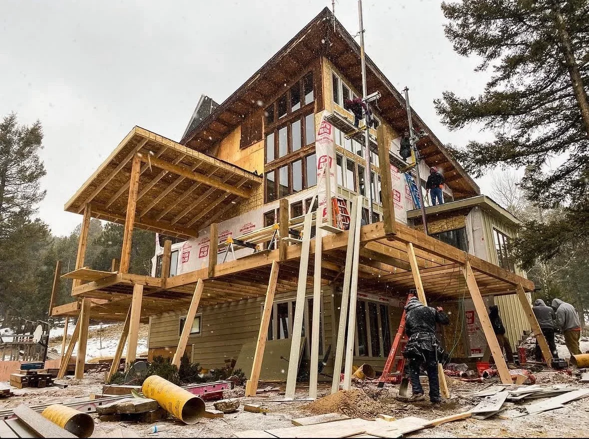 Timber frame home under construction with exposed wooden posts, beams, and multi-level deck framing