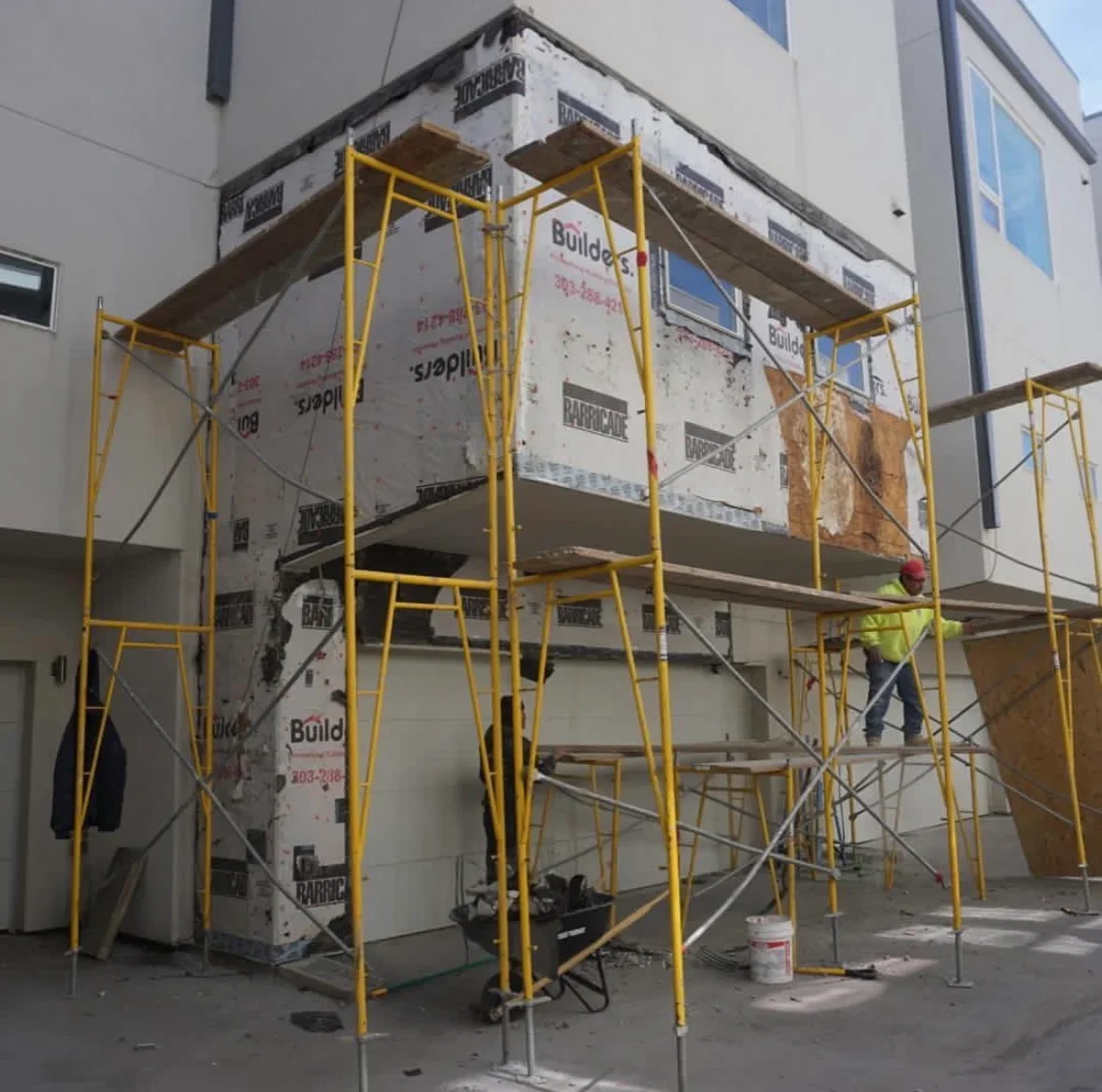 Commercial building with yellow scaffolding, white house wrap, and weather barrier installation on multi-story facade