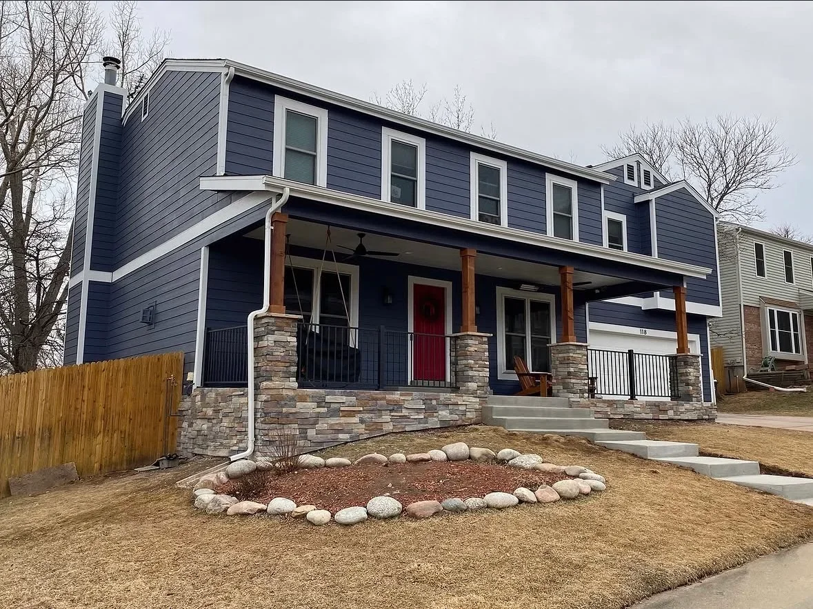 Dark blue house with stone veneer front porch, wooden posts, metal railings, concrete steps, and river rock landscaping