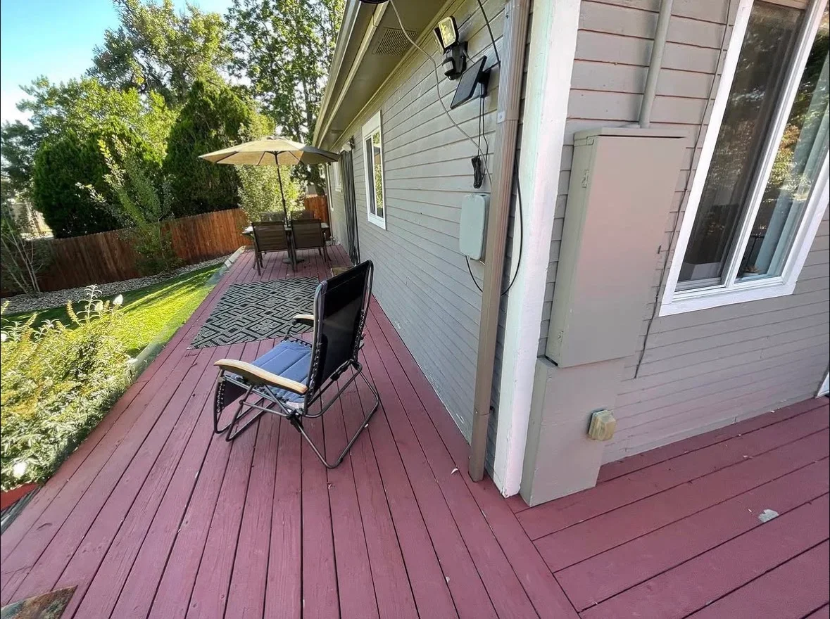 Burgundy composite deck with linear board pattern, patio furniture, and umbrella near house siding