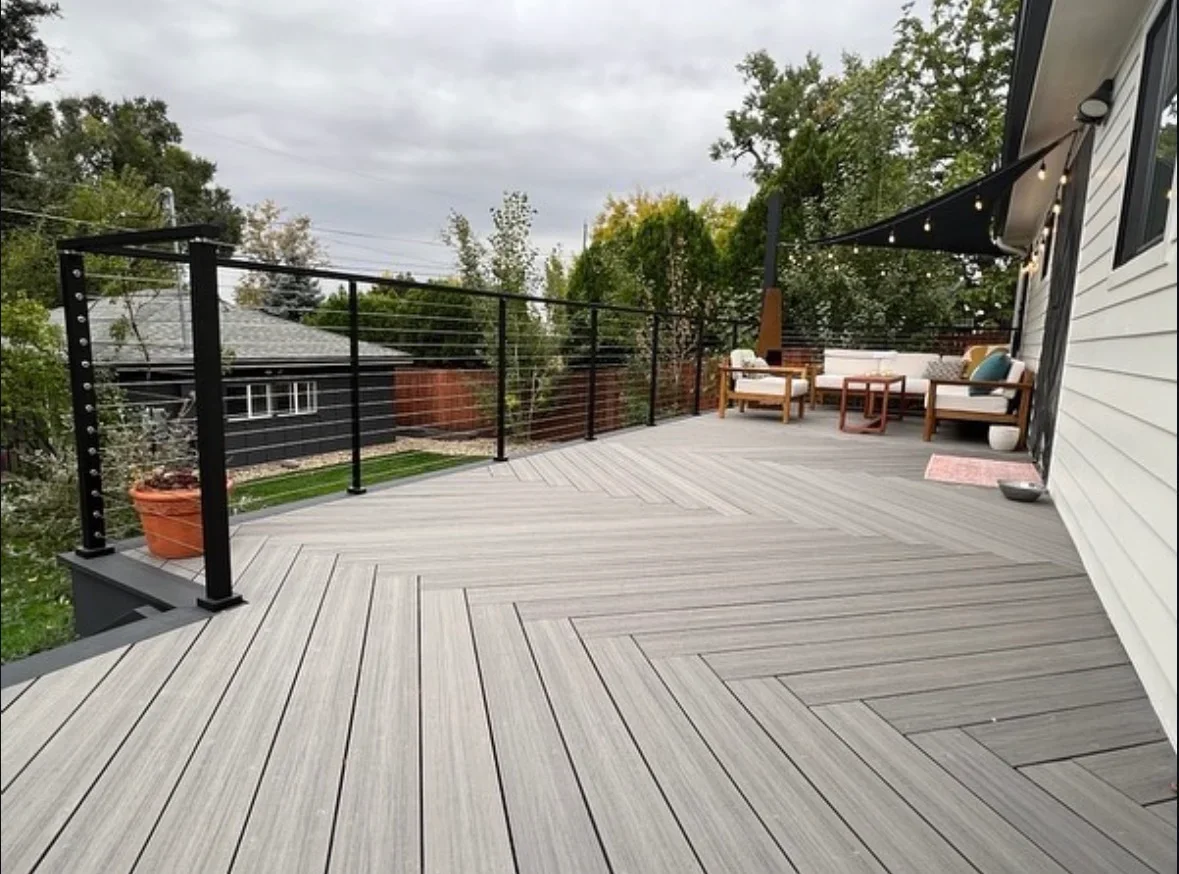 Gray composite deck with herringbone pattern, black steel cable railing, and modern pergola structure
