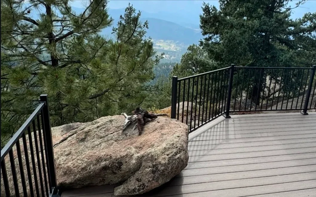 Gray composite deck with black metal railing overlooking mountain forest and boulder