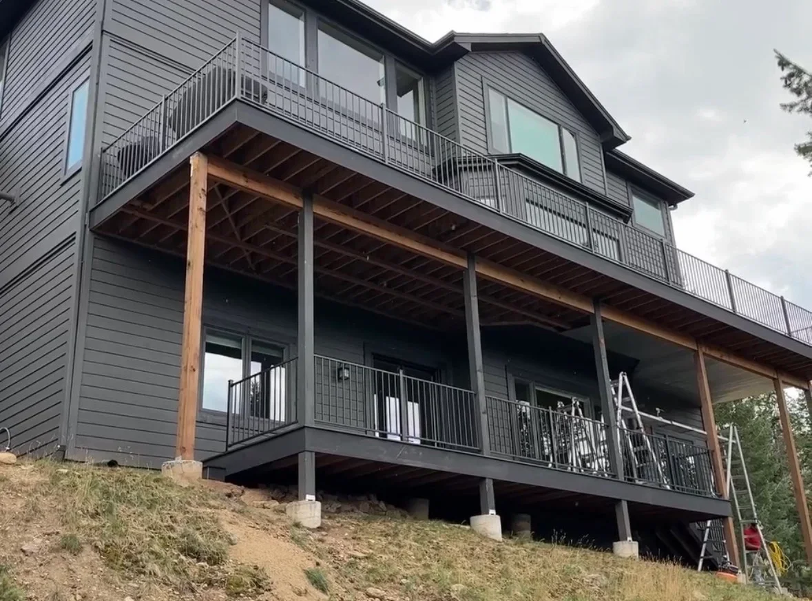 Two-level deck with timber beams, metal railings, and covered patio underneath on hillside home