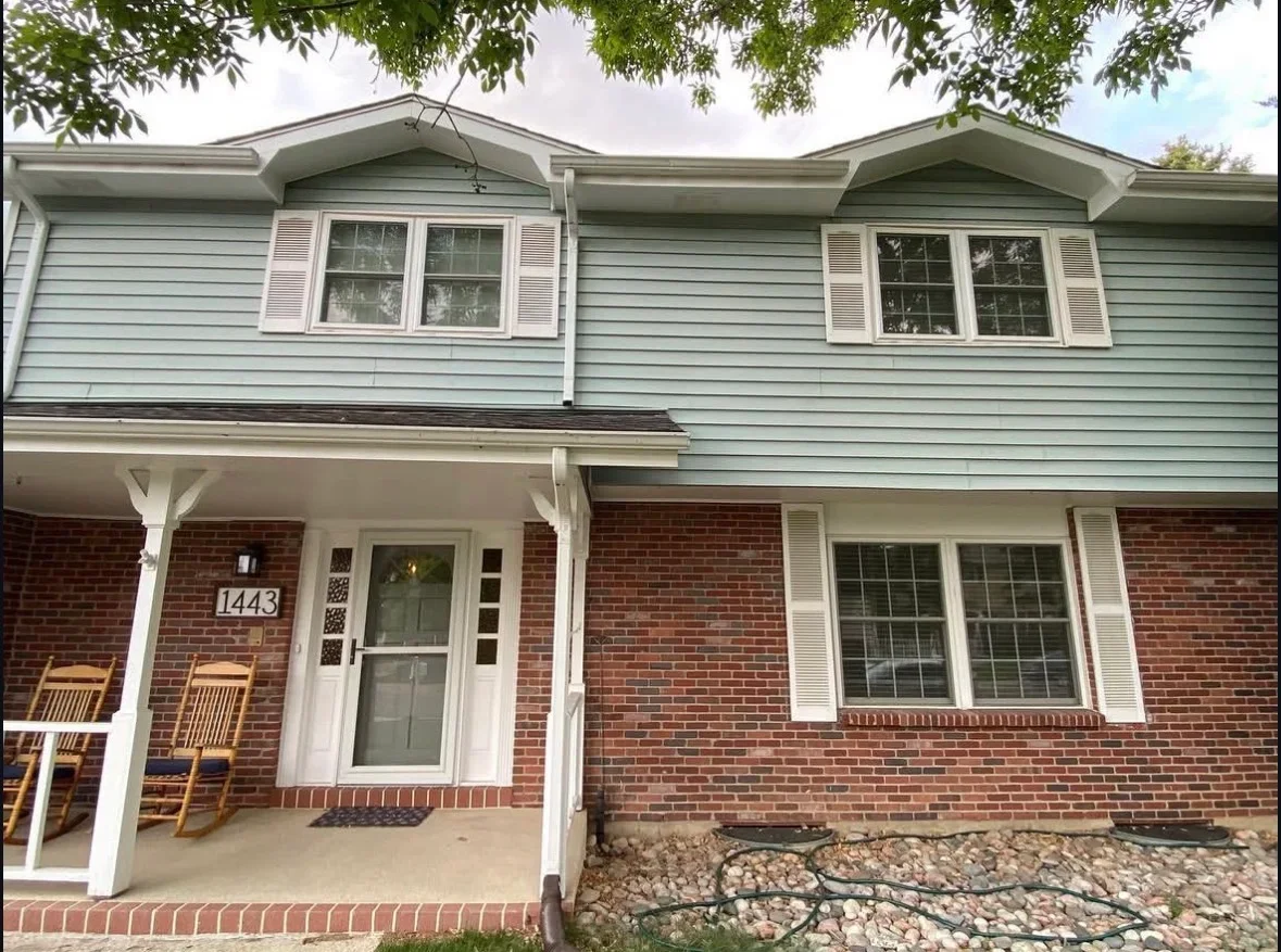 White covered porch with posts and beams on brick home with concrete pad