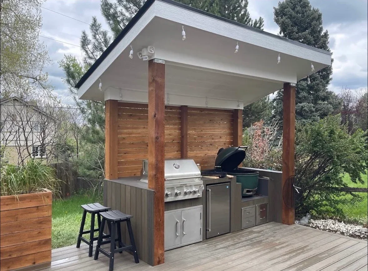 Outdoor kitchen pavilion with composite deck, timber posts, stainless steel grill, and horizontal wood screens