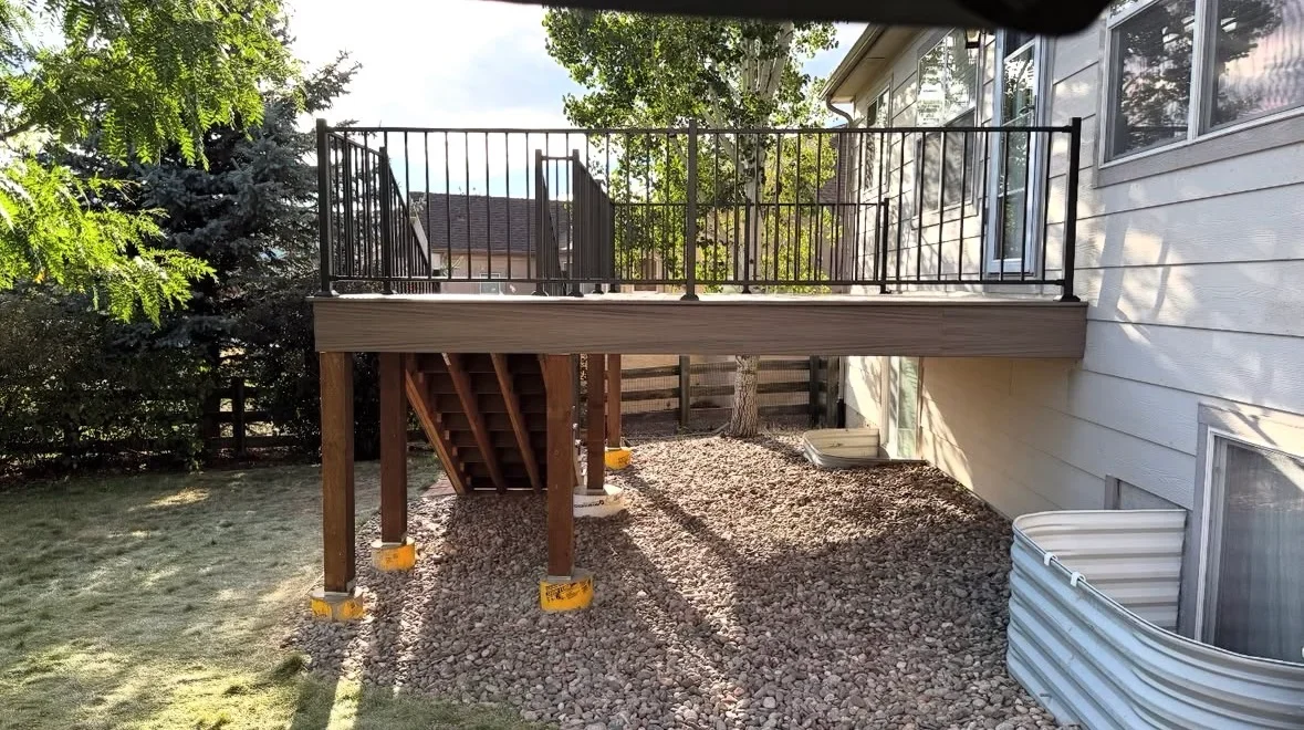 Elevated composite deck with black metal railing, wooden support posts, and gravel under-deck area