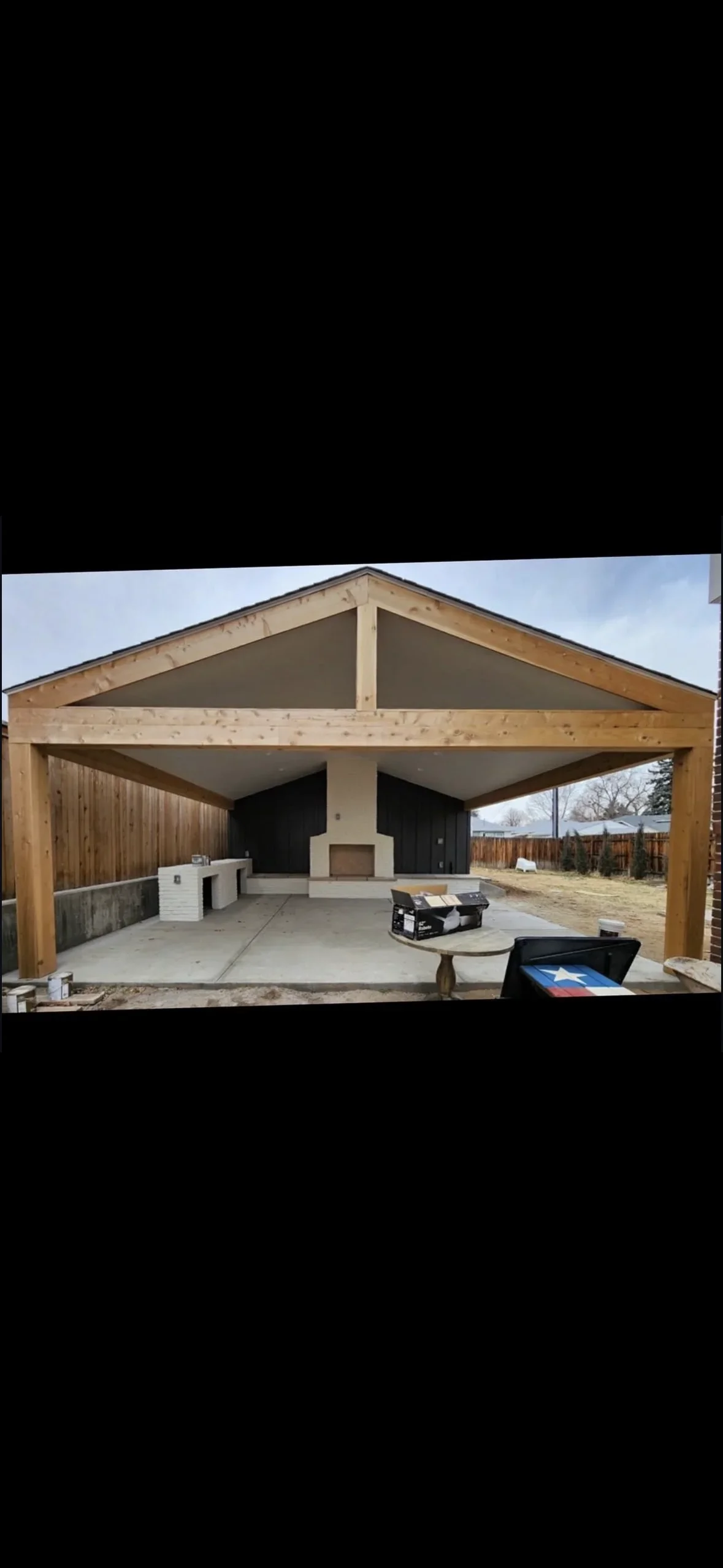 Timber pavilion with gable roof, wooden beams, concrete patio, and built-in fireplace