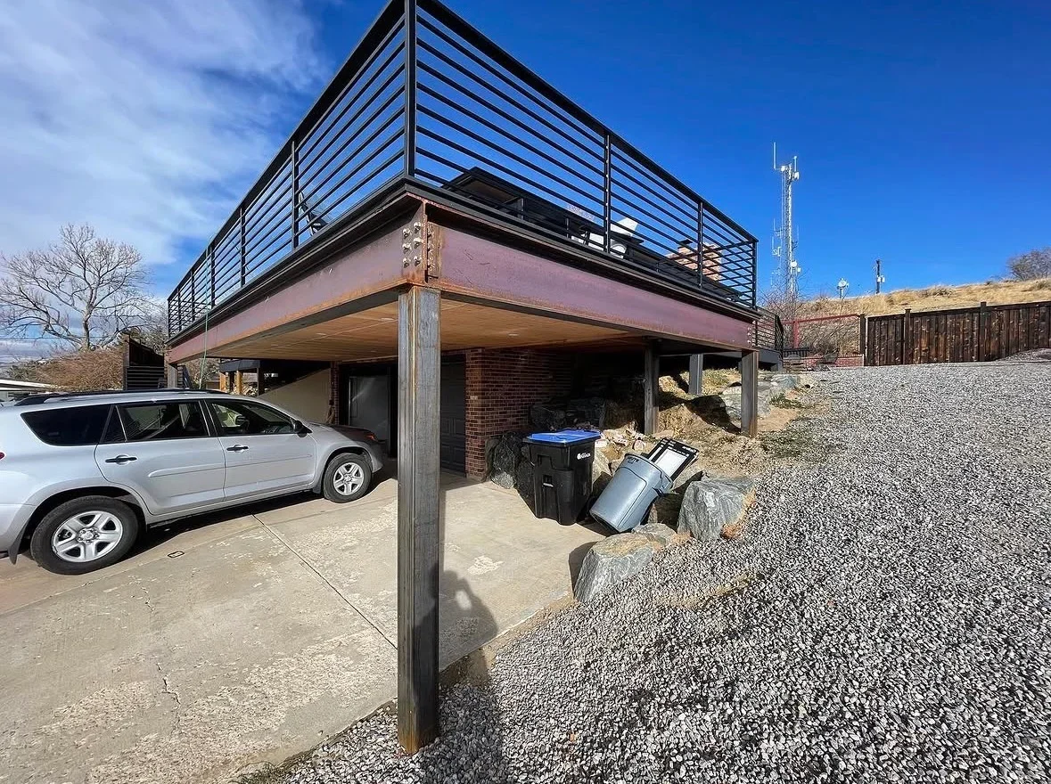 Elevated deck with metal railings, composite decking, and covered carport with brick columns