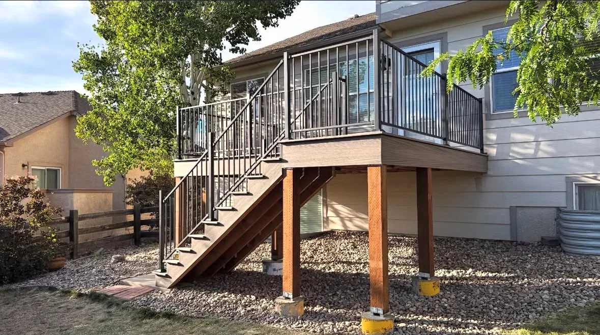 Elevated wood deck with black metal railing, stairs, and brick support posts over gravel base