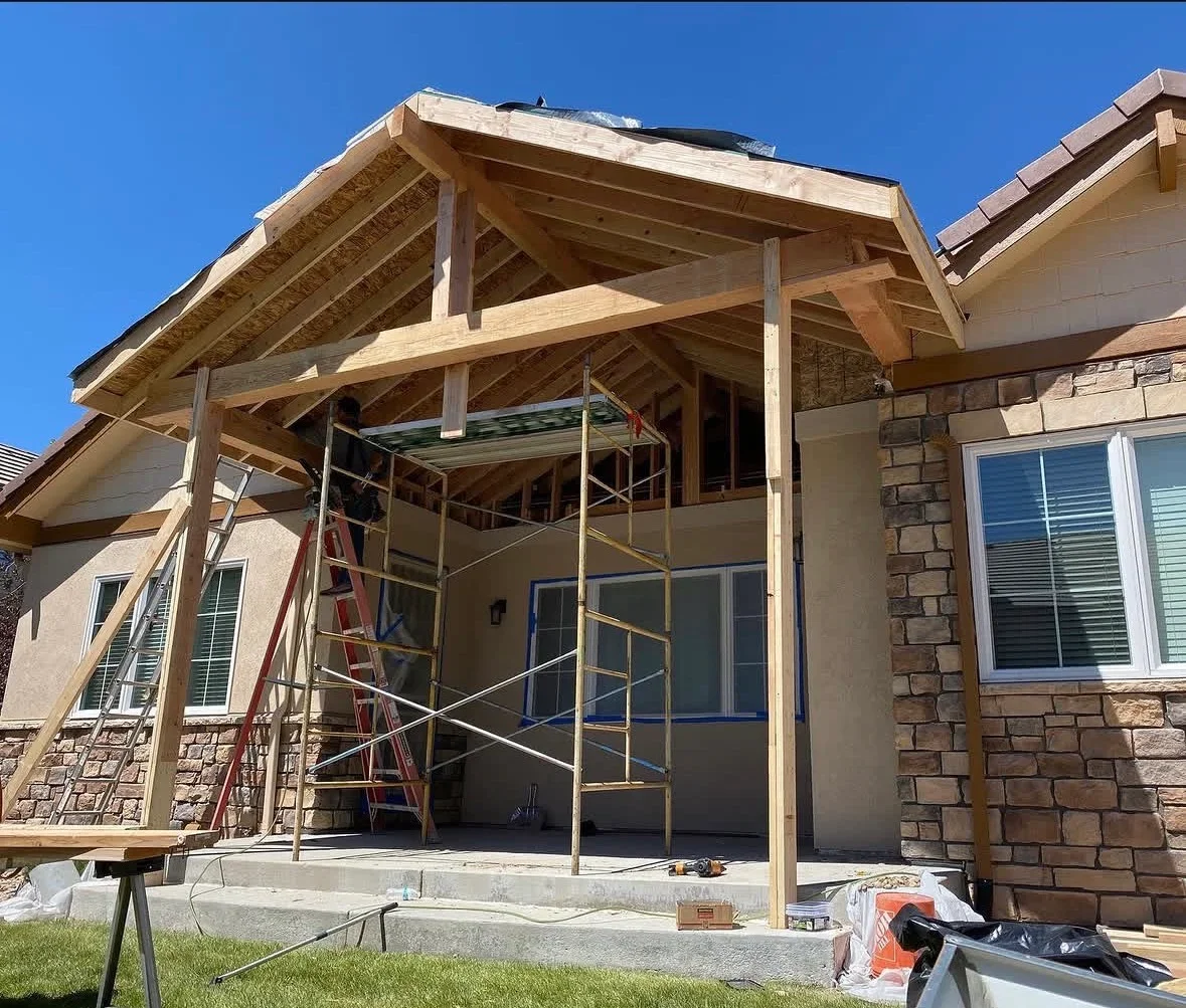 Timber frame patio cover with exposed beams, gable roof, and stone veneer home