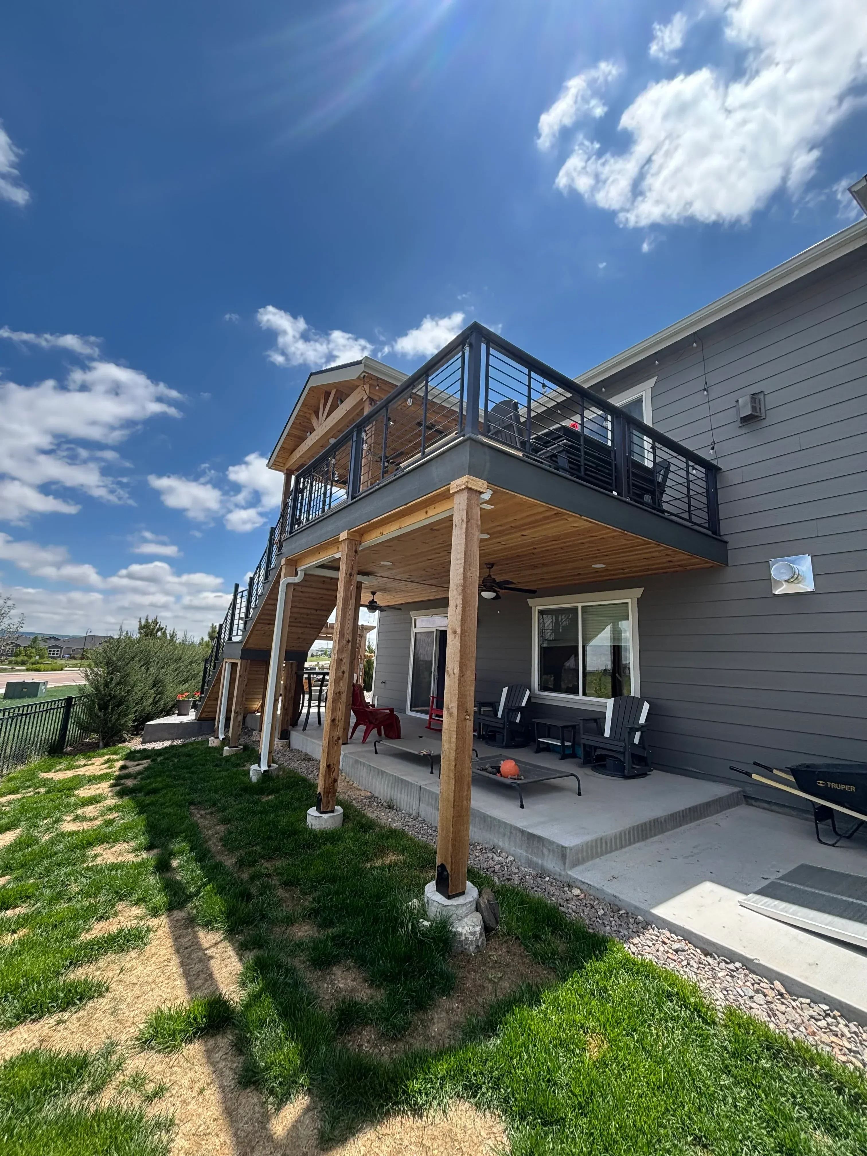 Multi-level wood deck with black metal railing and wooden posts against house