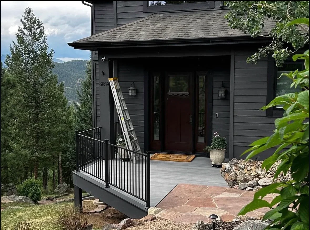 Gray composite deck with black metal railing, stone patio, and mountain views