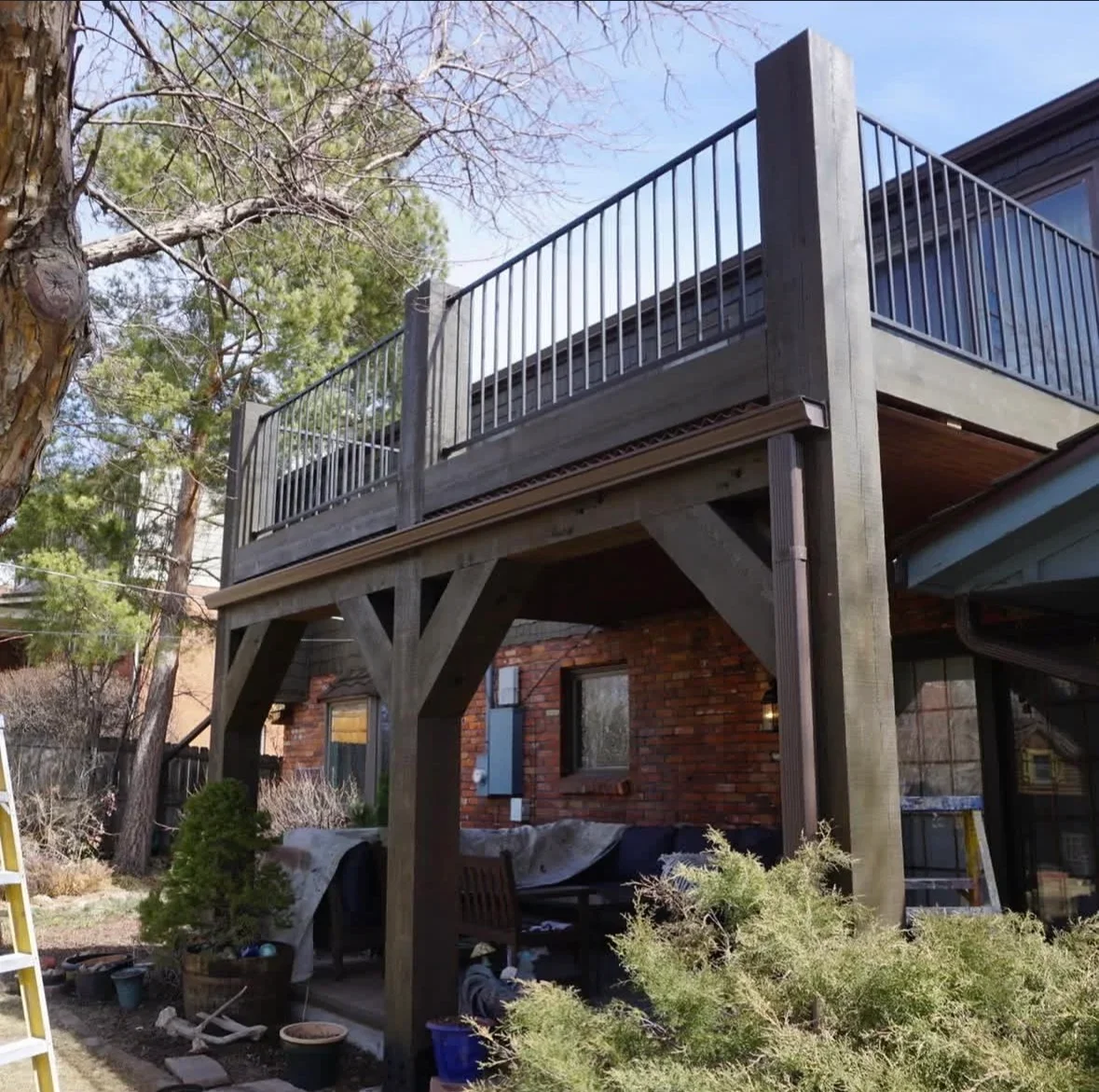 Elevated wooden deck with metal railing attached to brick home with timber support posts