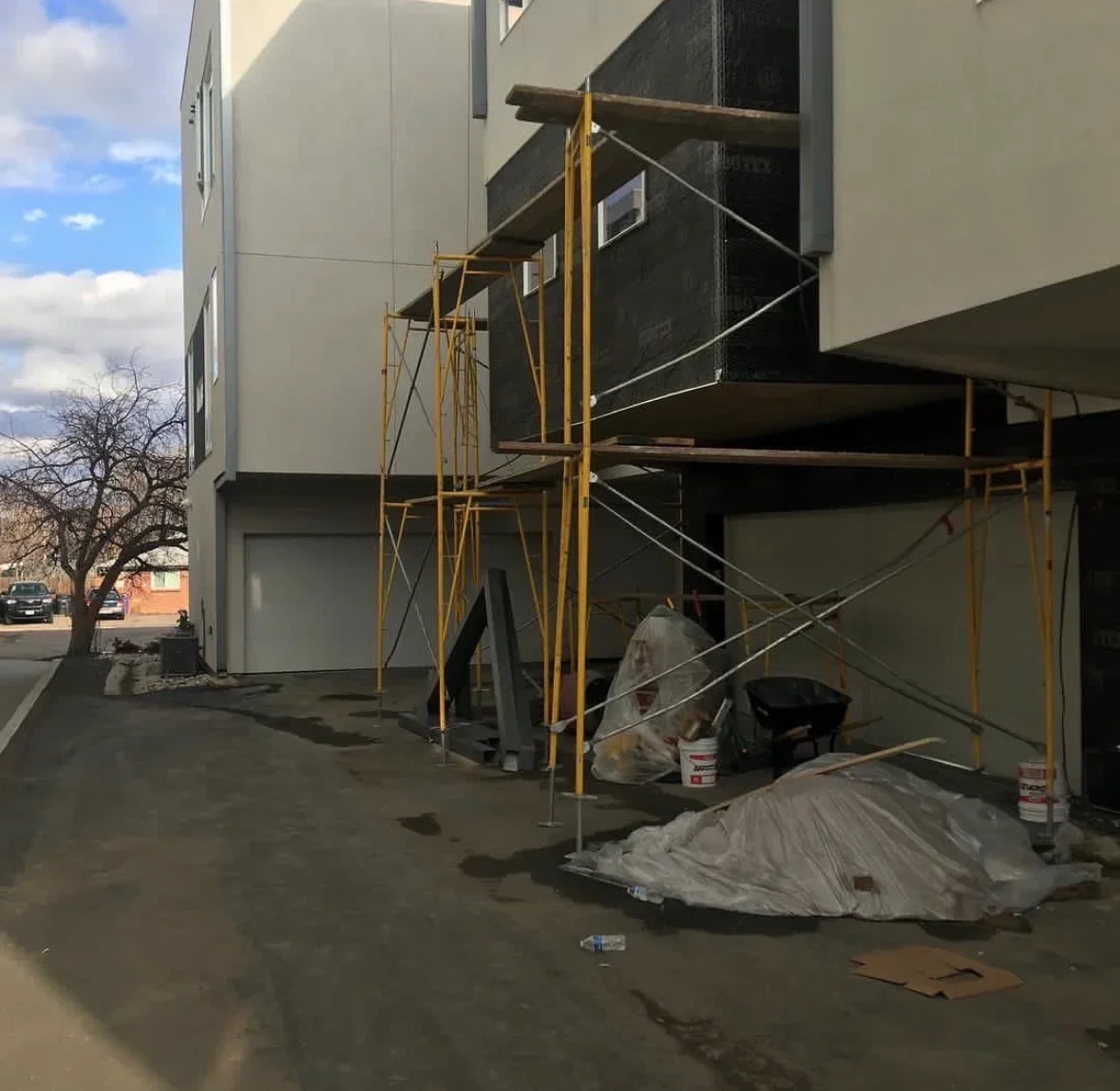 Steel stair tower with cable railings and yellow scaffolding on concrete pad during commercial exterior work
