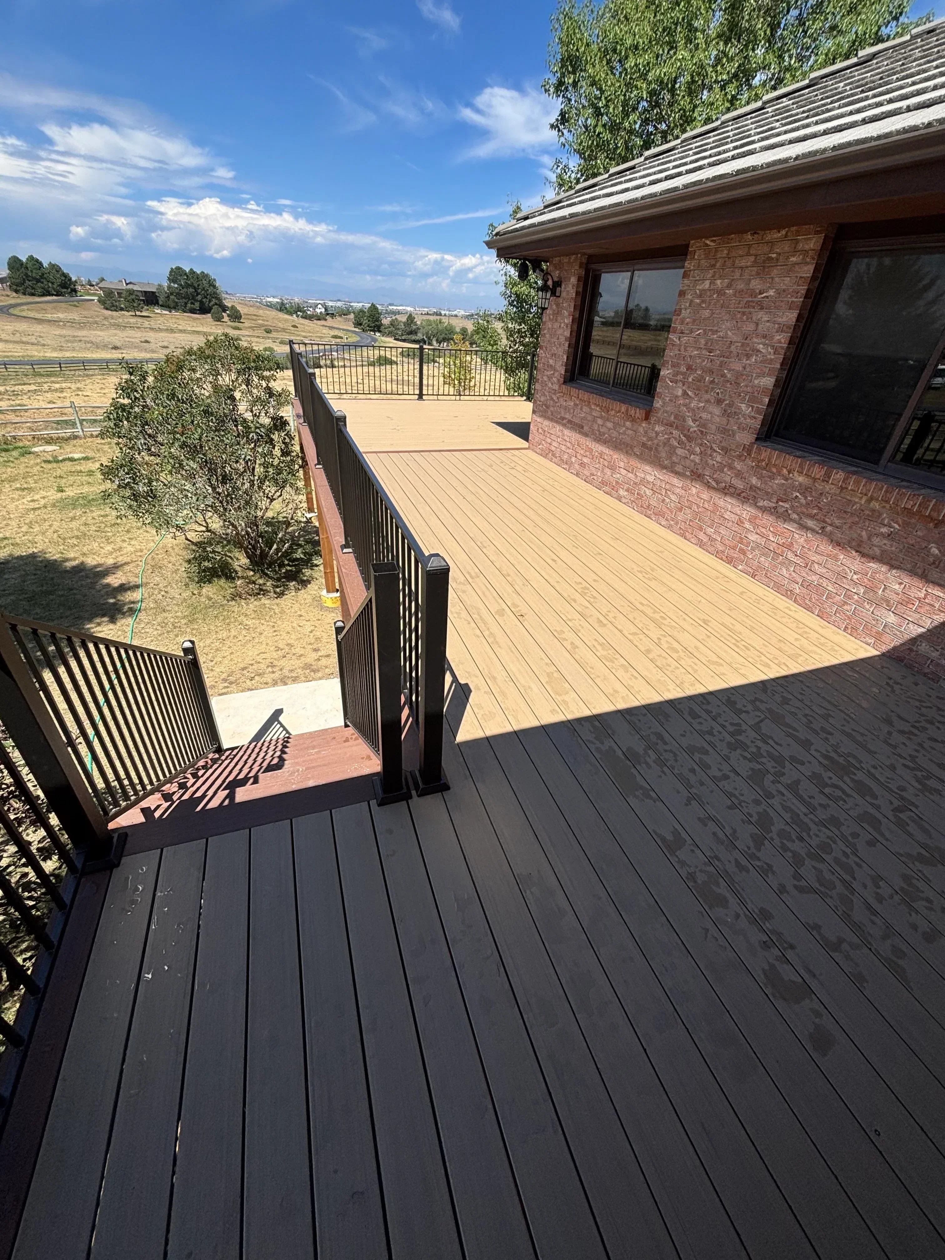 Black metal deck with horizontal slat railings and shade pergola attached to brick home with new siding