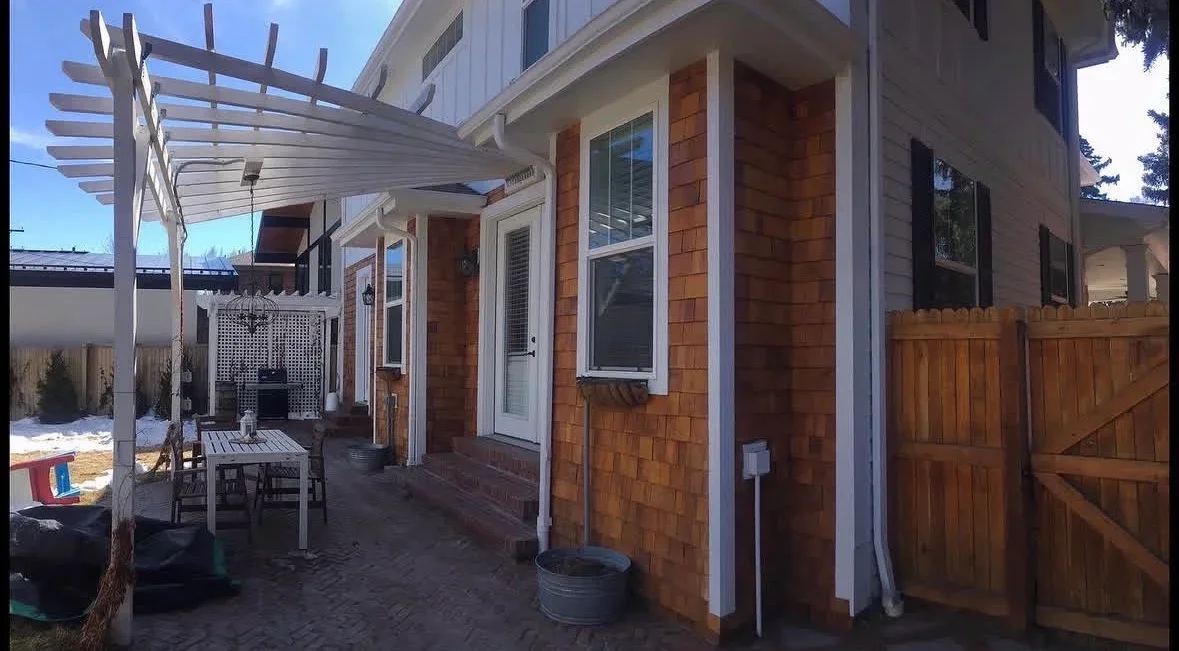 White pergola over patio with cedar shake siding and wooden gate