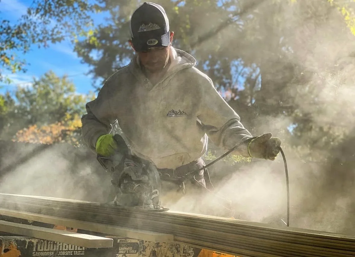 Worker pressure washing wooden deck with high-powered equipment, creating visible dust and debris clouds