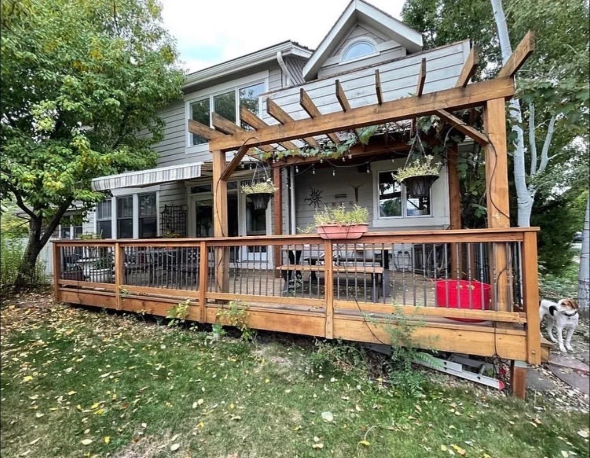 Wooden deck with metal railing and timber pergola attached to house exterior