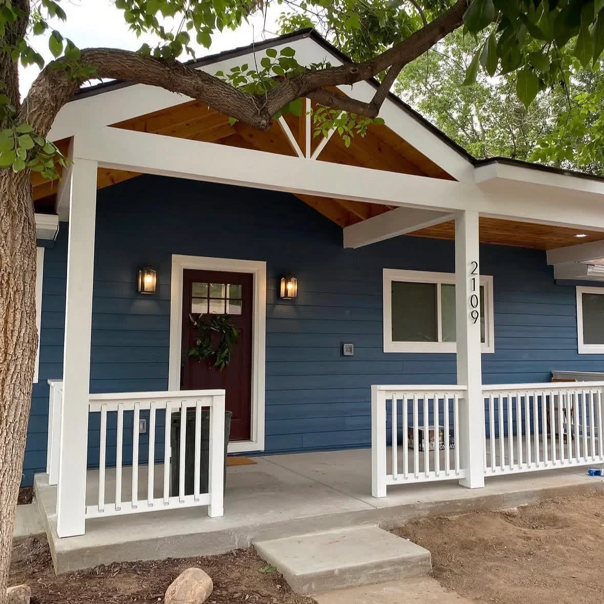 Covered porch with white railings, exposed wood beams, and concrete pad