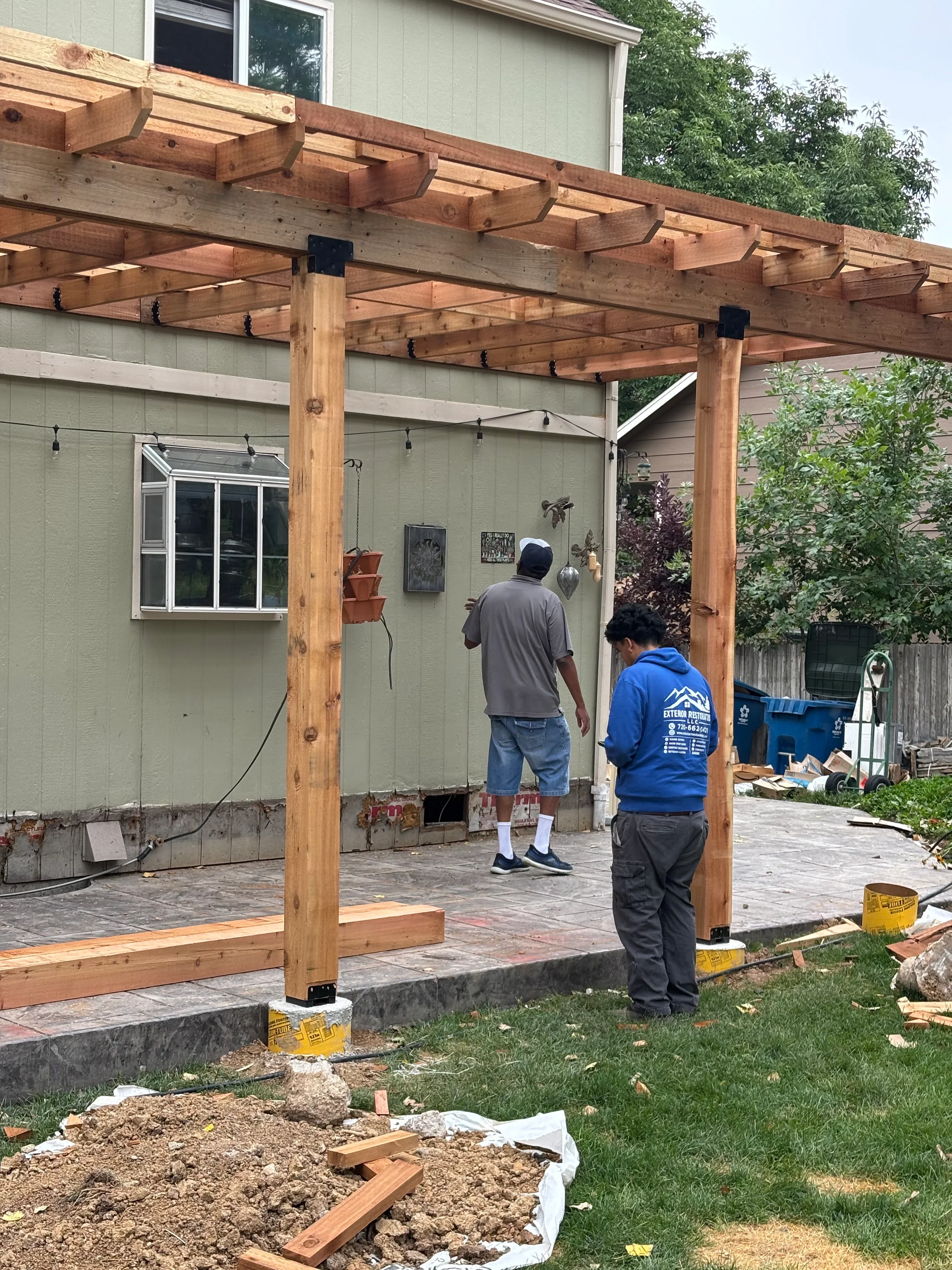Cedar pergola with curved brackets and timber posts over paver patio during installation