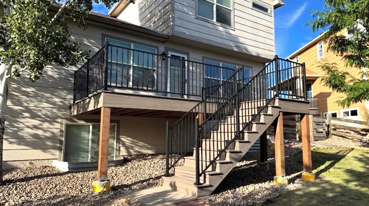 Two-level composite deck with black metal railings, glass panels, and wooden support posts
