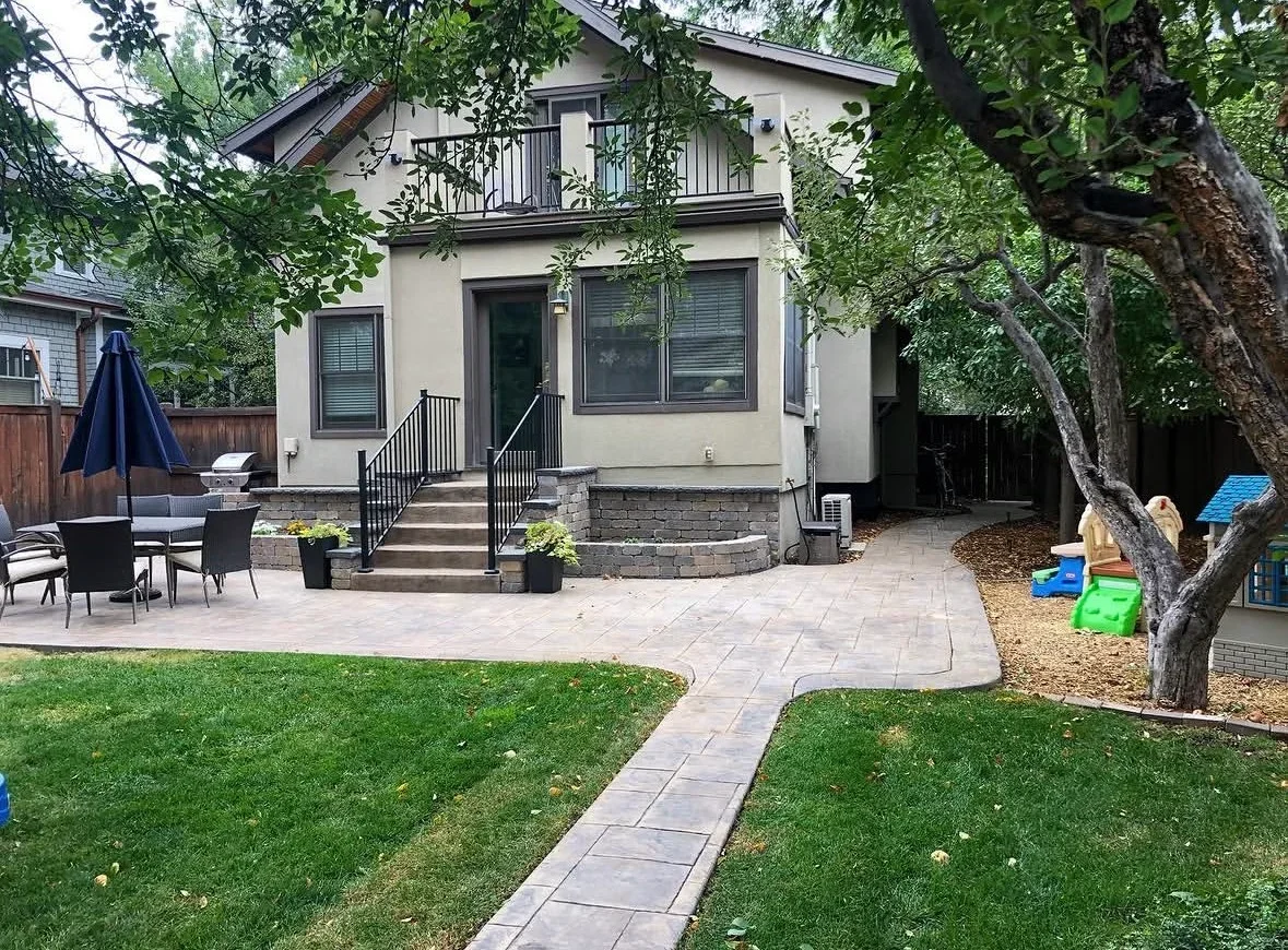 Gray paver patio with stone veneer base, metal railings, and lawn walkway