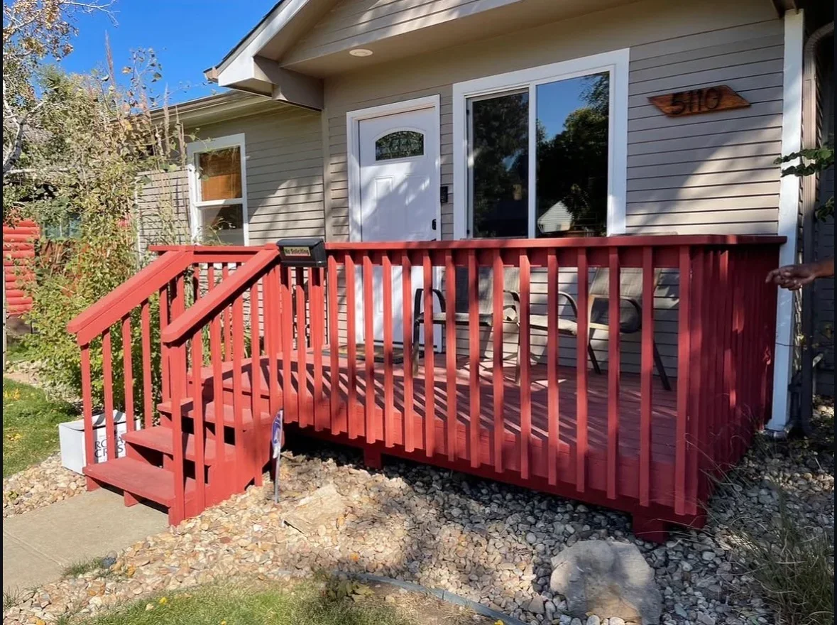 Red composite deck with vertical balusters, white-trimmed stairs, and river rock base