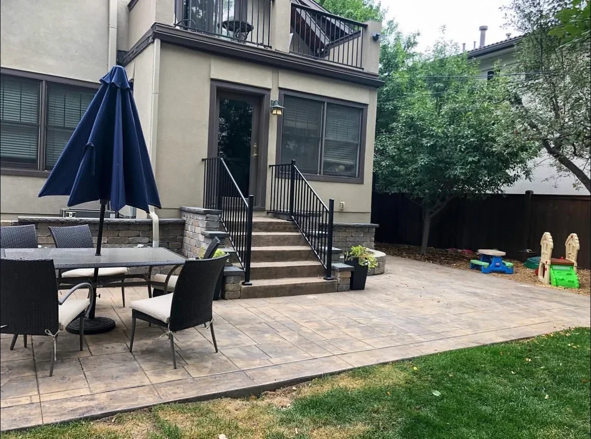 Large paver patio with stone retaining wall, metal railing, and integrated steps leading to elevated deck