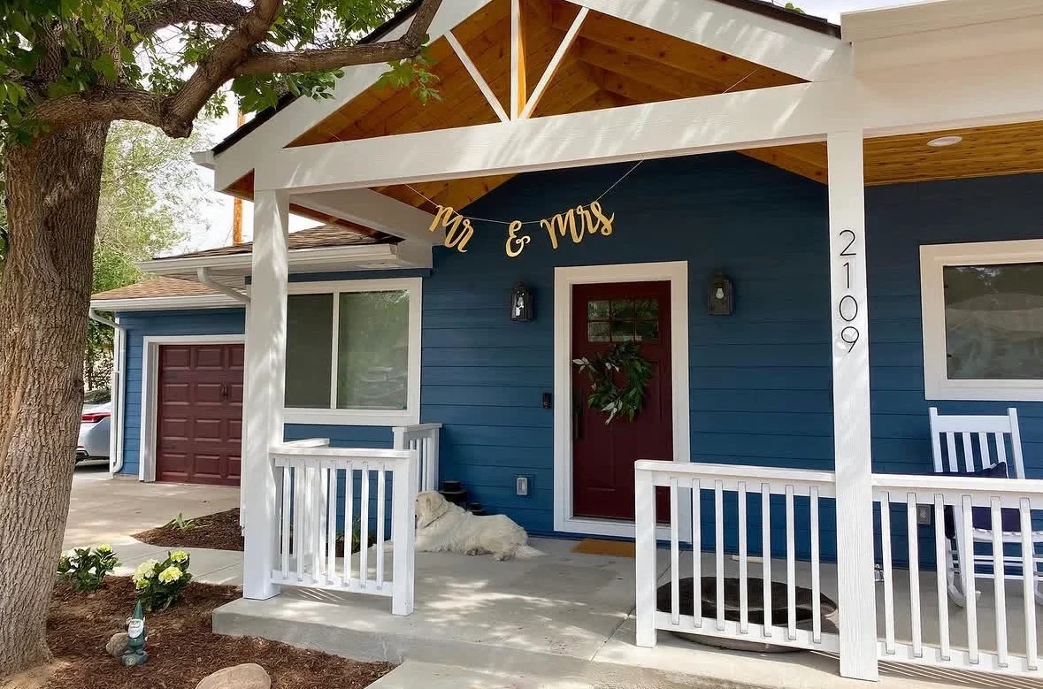 White covered porch with exposed wood beams, white railings, and concrete patio foundation