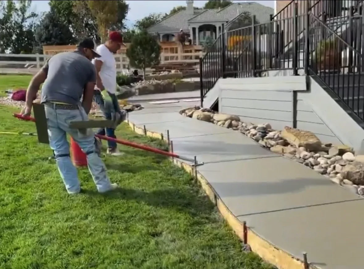 Concrete patio construction with stone edging, river rock borders, and black metal railing installation