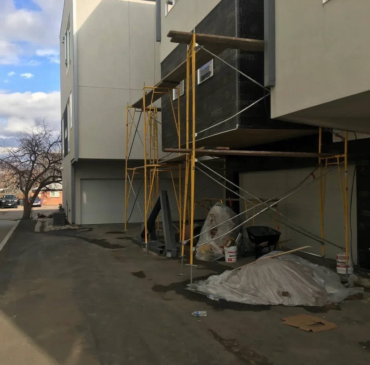 Commercial building exterior with yellow metal scaffolding, concrete patio, and protective coverings during renovation