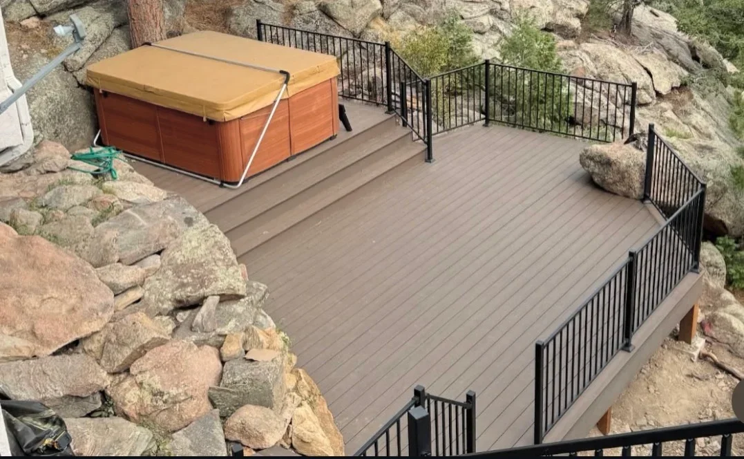 Gray composite deck with black aluminum railings on hillside, hot tub with gold cover