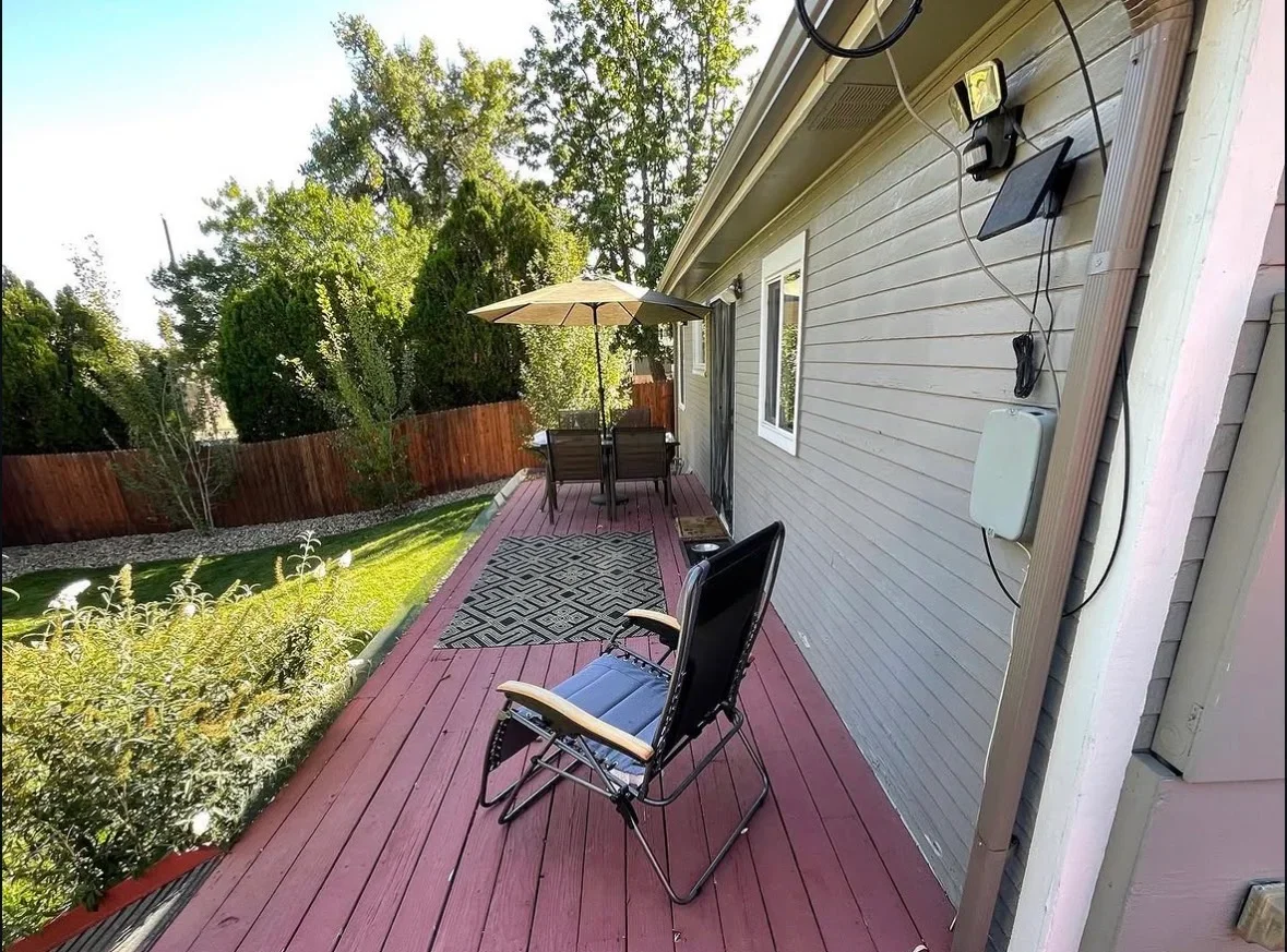 Composite deck with burgundy boards, patio furniture, umbrella, and geometric rug adjacent to house siding