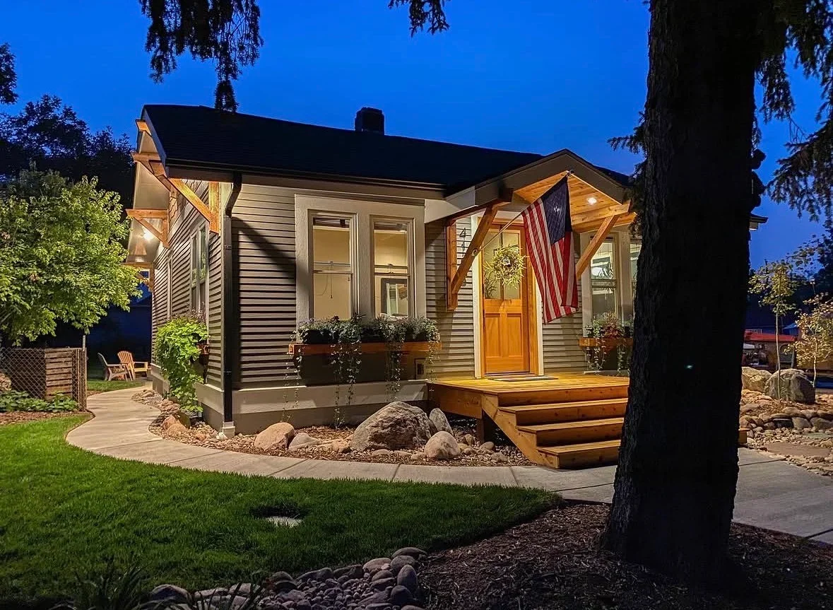 Illuminated wood deck with timber pergola, concrete patio, and stone landscaping at twilight