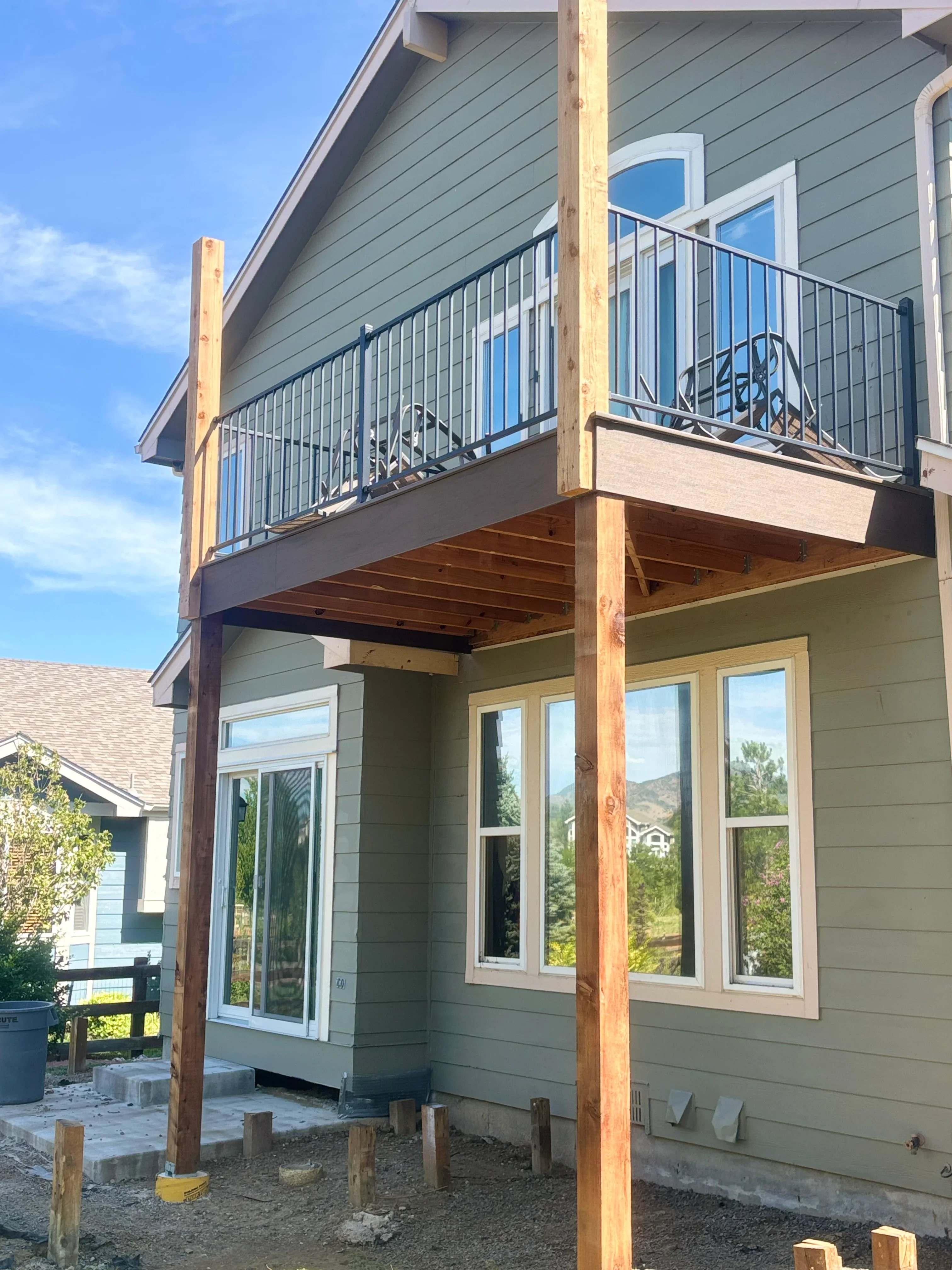 Elevated wood deck with black metal railing and horizontal cables, attached to house with large windows