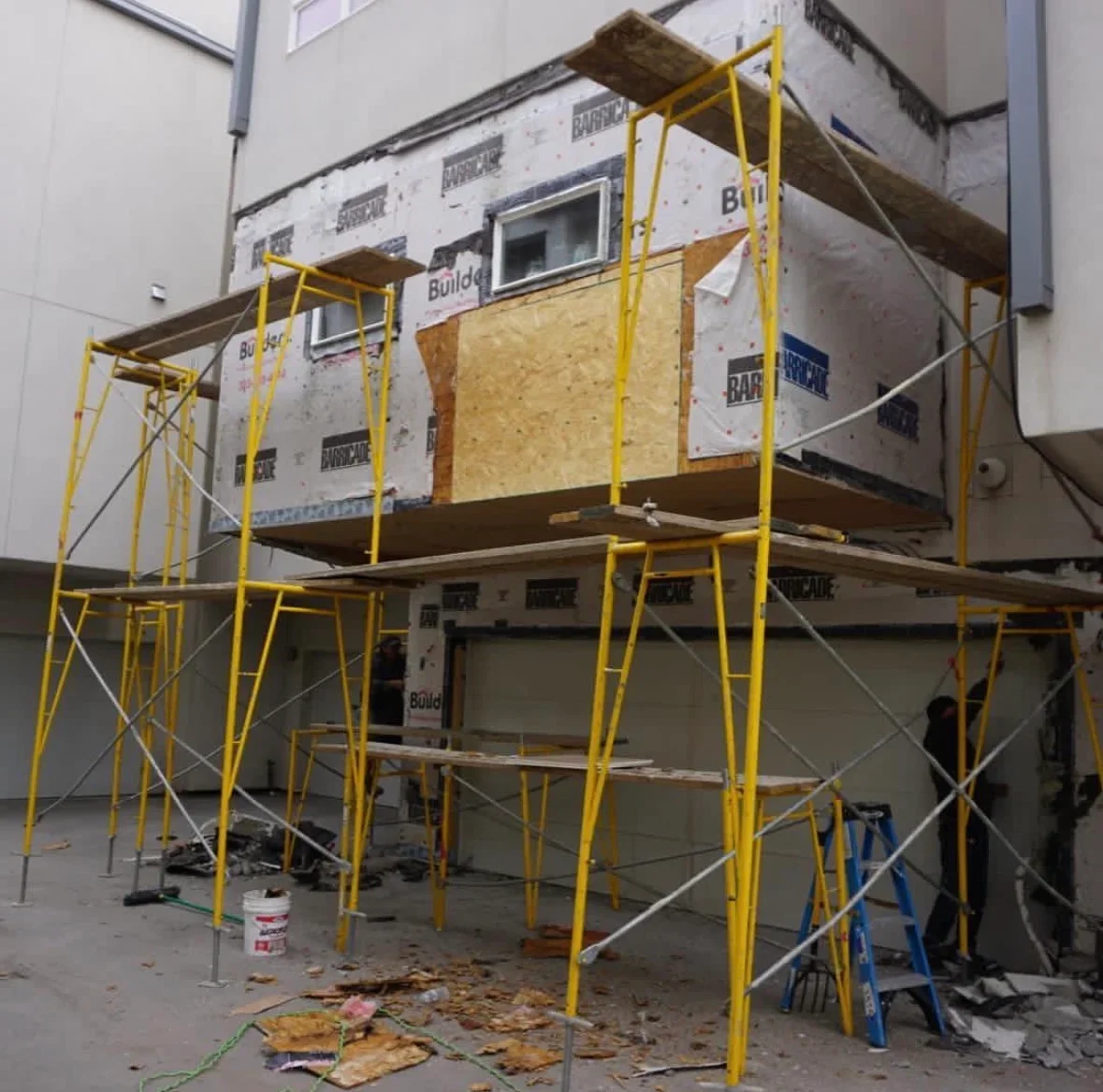 Multi-story building facade with yellow scaffolding, house wrap, and OSB sheathing installation