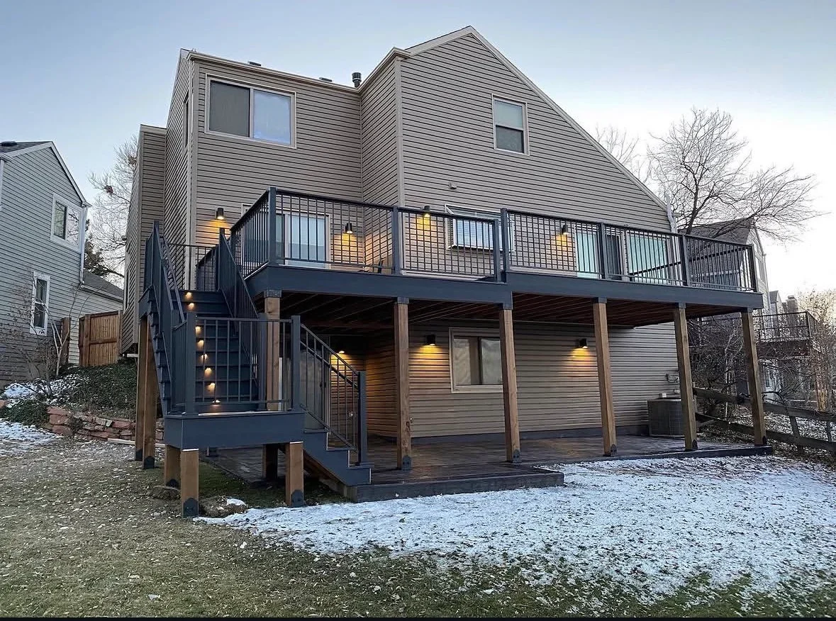 Two-level composite deck with metal railing, wooden posts, and integrated lighting on residential home