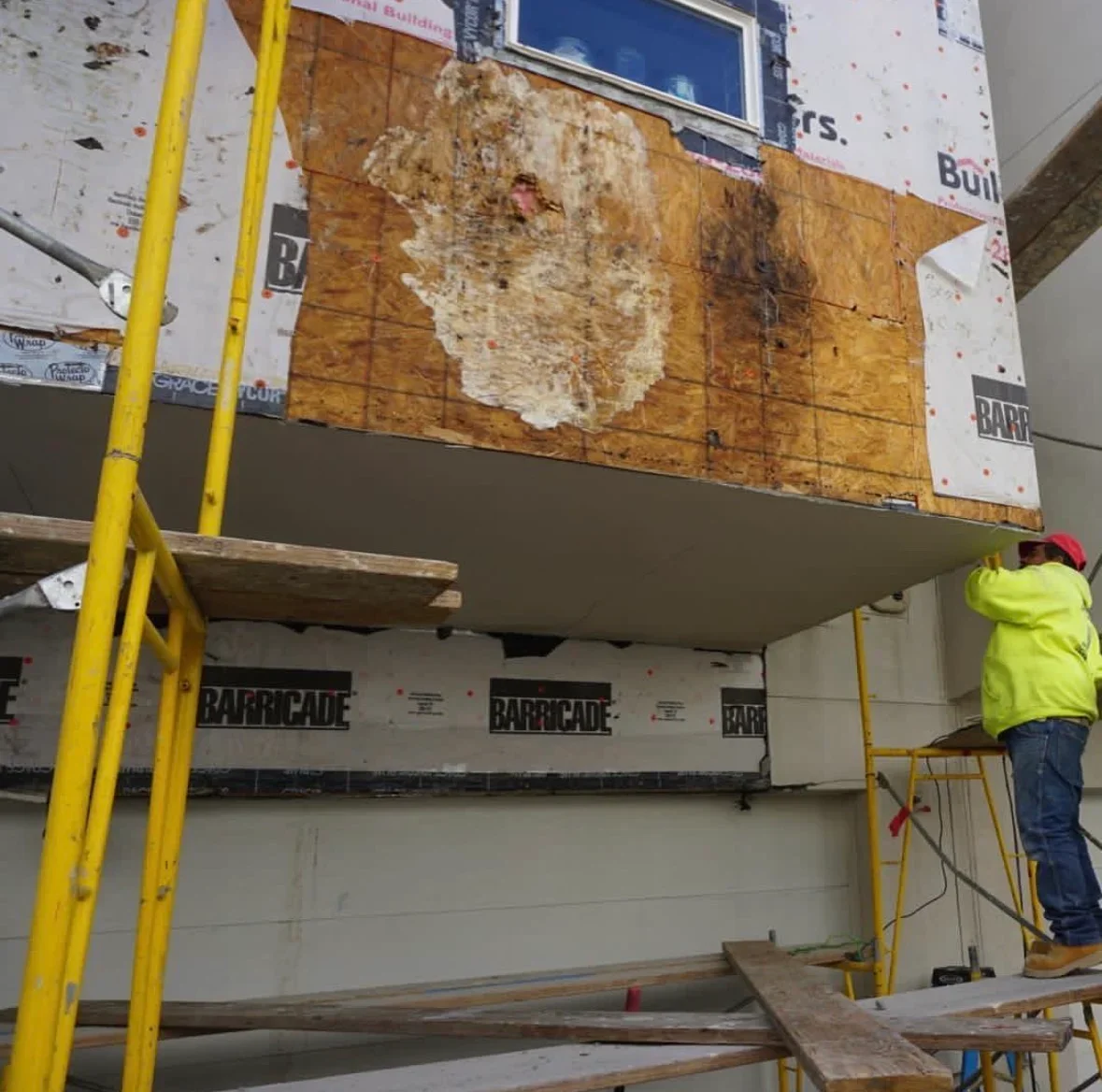 Worker installing new soffit and ceiling materials with yellow ladder and Barricade moisture barrier visible