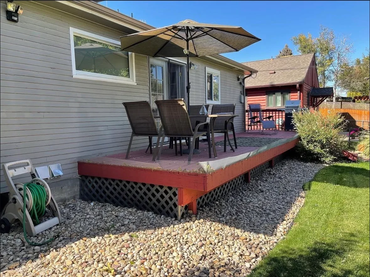 Elevated deck with red composite frame, black lattice skirting, and surrounding gravel landscaping