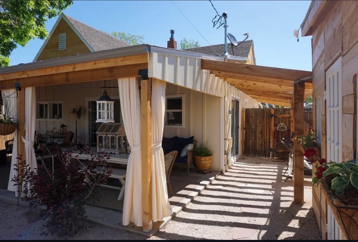 Wooden pergola patio with exposed beams, white curtains, and striped concrete flooring