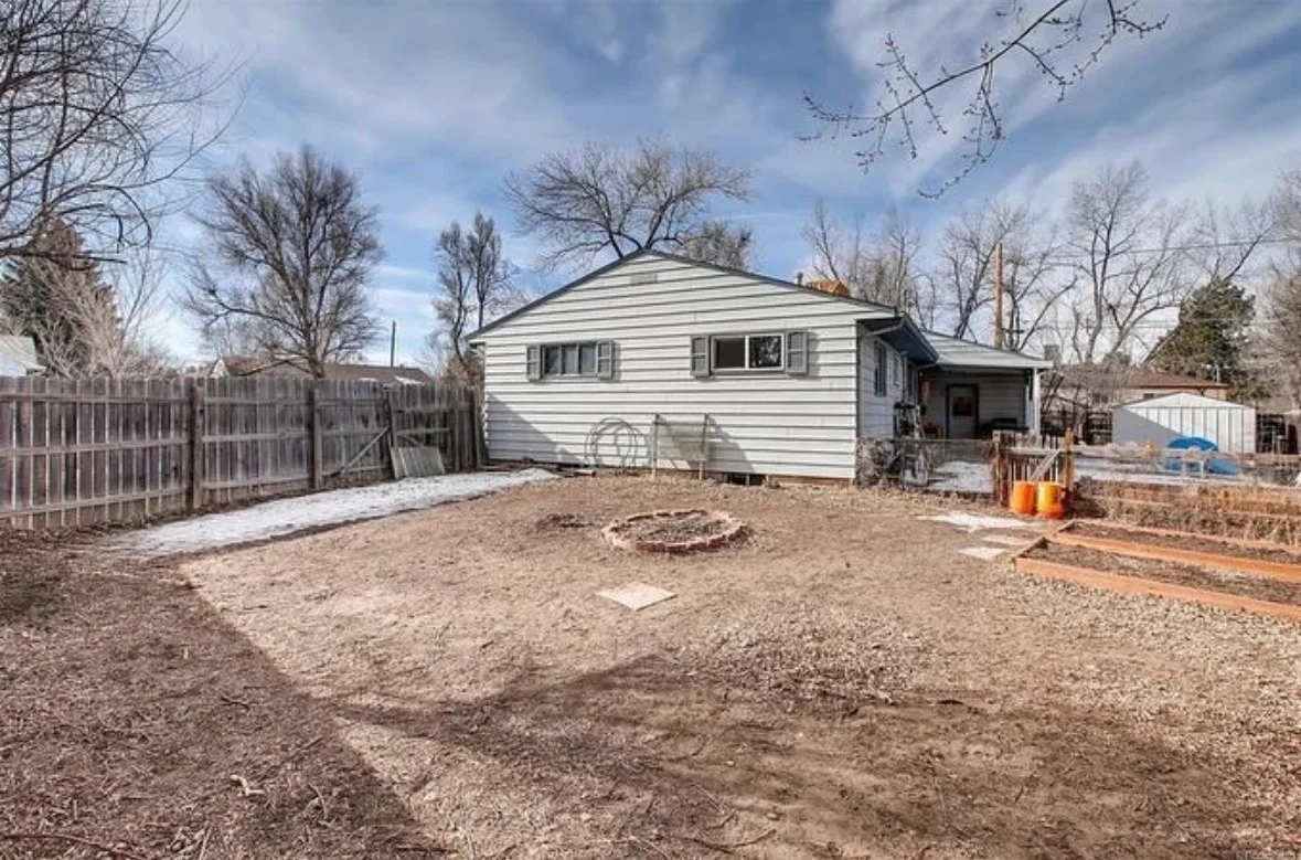 Graded dirt backyard with wooden fence, single-story white siding house, and fire pit area