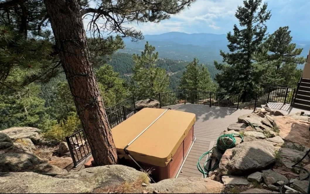 Composite deck with hot tub, metal railings, and mountain valley views through pine trees