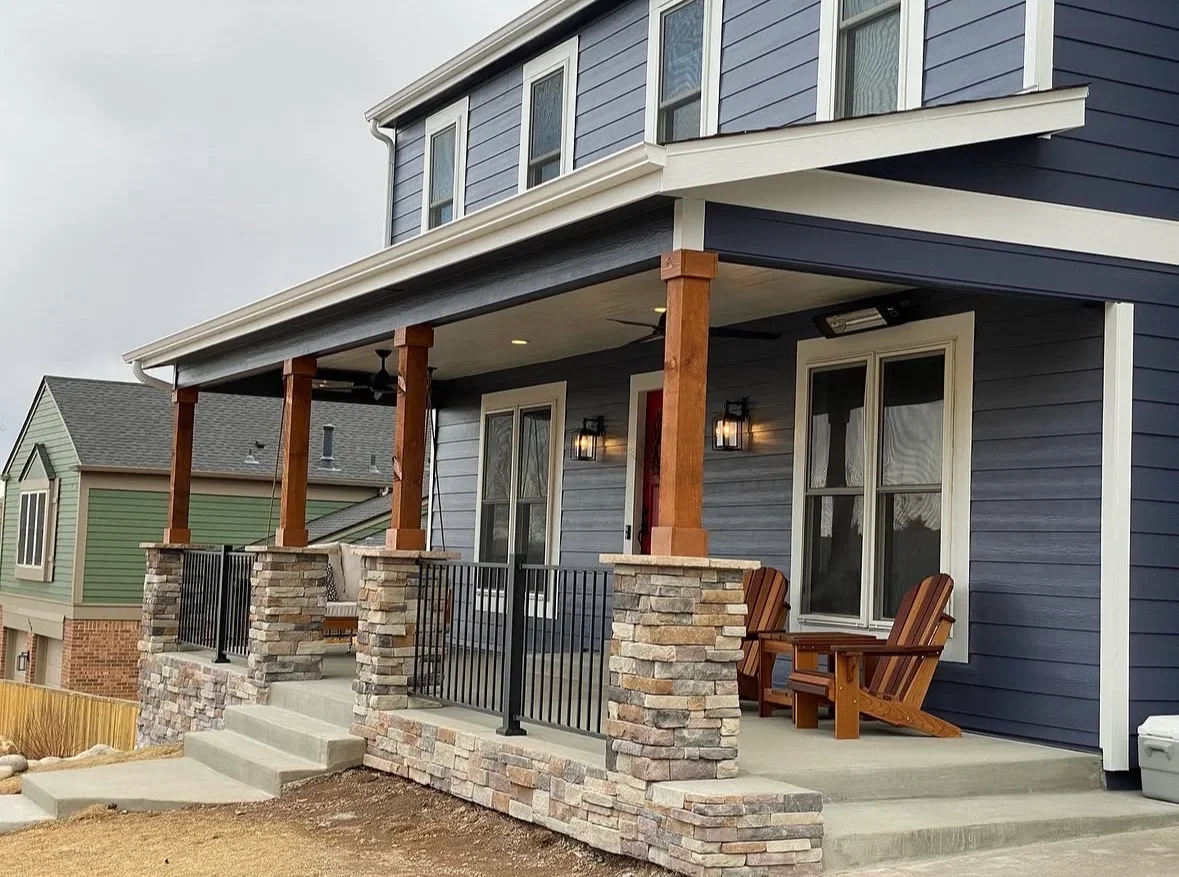 Front porch with stone pillars, cedar posts, black metal railings, and concrete pad