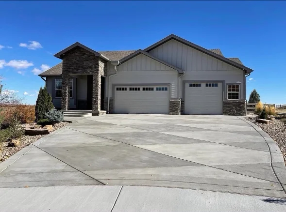 Freshly poured concrete driveway at a residential property in Littleton, Colorado, with clean edging and a smooth surface finish. The installation shows proper slope and joint placement suited to the surrounding yard grade.