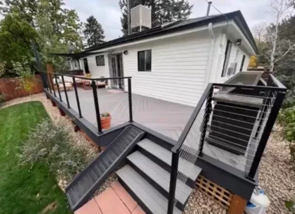 A newly installed wood-framed deck with composite decking boards attached to the back of a single-story home in Littleton, Colorado, with a sloped backyard and foothills visible in the background. The deck includes code-compliant railings and a stair landing leading to the yard below.