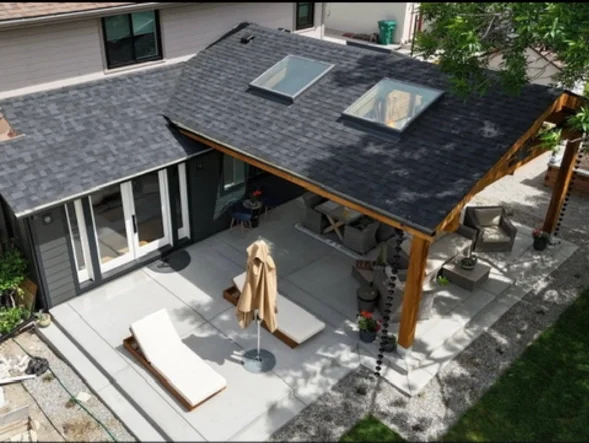 A newly installed attached patio cover on a Littleton, Colorado home, showing solid overhead framing and clean trim work integrated with the home's existing roofline. The covered patio extends over a backyard deck with open views of the surrounding Colorado Front Range landscape.